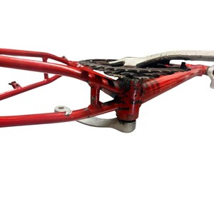 Puede incluir: Un cuadro de bicicleta rojo con un conjunto de cadena y engranajes. El cuadro es de metal y tiene un dise&ntilde;o curvo. La cadena y los engranajes son negros y plateados. El cuadro parece ser vintage o usado.