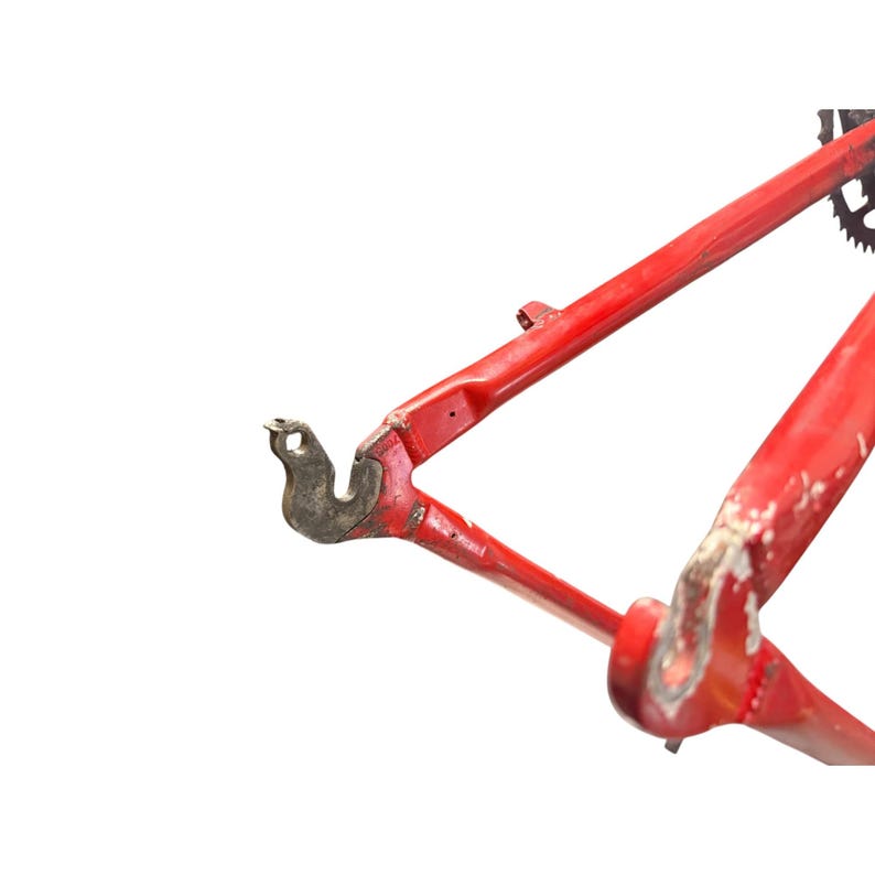 Puede incluir: Una secci&oacute;n de un cuadro de bicicleta rojo, que muestra el tri&aacute;ngulo trasero y la puntera. El cuadro tiene desgaste visible, con algunas zonas donde la pintura est&aacute; desconchada o falta. El metal tiene un aspecto ligeramente desgastado.