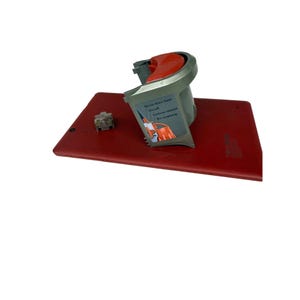Peut inclure: Une base rectangulaire rouge avec un composant d'aspirateur gris et rouge. Le composant a une poignée rouge et une étiquette avec du texte. Un petit composant carré gris est sur la base. Le composant de l'aspirateur a un tuyau à tirage rapide.