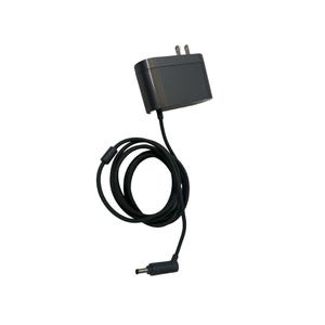 Puede incluir: Un adaptador de corriente gris oscuro con un cable negro y un enchufe de dos clavijas. El cable está enrollado y tiene un conector en el extremo. El adaptador es rectangular y tiene un acabado liso. El fondo es blanco.