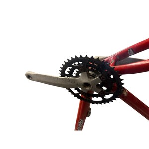 Puede incluir: Un juego de bielas de bicicleta con un plato negro y una biela plateada est&aacute; unido a un cuadro de bicicleta rojo. El plato tiene m&uacute;ltiples dientes y est&aacute; dise&ntilde;ado para una transferencia de potencia eficiente. El cuadro muestra signos de desgaste.