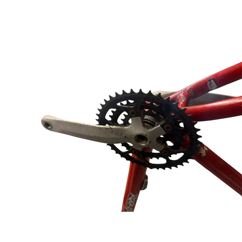 Puede incluir: Un juego de bielas de bicicleta con un plato negro y una biela plateada est&aacute; unido a un cuadro de bicicleta rojo. El plato tiene m&uacute;ltiples dientes y est&aacute; dise&ntilde;ado para una transferencia de potencia eficiente. El cuadro muestra signos de desgaste.