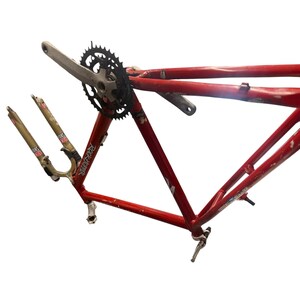 Puede incluir: Un cuadro de bicicleta de monta&ntilde;a rojo con un plato y biela negros. Las horquillas de suspensi&oacute;n delantera son doradas y tienen el texto "Rock Shox" impreso. El cuadro tiene el texto "Rockhopper" impreso.
