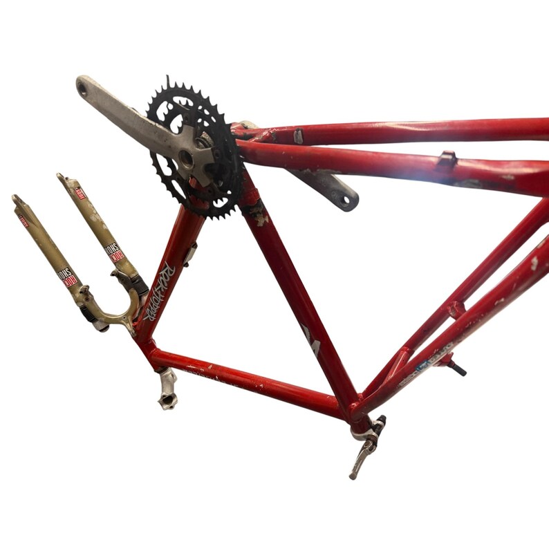 Puede incluir: Un cuadro de bicicleta de monta&ntilde;a rojo con un plato y biela negros. Las horquillas de suspensi&oacute;n delantera son doradas y tienen el texto "Rock Shox" impreso. El cuadro tiene el texto "Rockhopper" impreso.