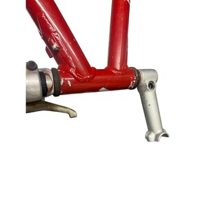 Puede incluir: Primer plano de un cuadro de bicicleta rojo con componentes plateados. El cuadro muestra signos de desgaste, con ara&ntilde;azos y desconchones de pintura visibles. Los componentes plateados incluyen una biela y un pedalier.
