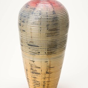 May include: A tall, ceramic vase with a rounded, bulbous shape. The vase is decorated with a light brown glaze and has a textured, ribbed surface. The top of the vase is a light pink color.