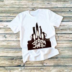 Pode incluir: Camiseta branca com uma estampa gráfica em preto e branco de um grupo de pessoas em pé na frente de um conjunto de facas e armas de fogo. O texto "From Hell" está escrito em uma fonte estilizada abaixo do gráfico.