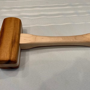 May include: A wooden mallet with a light brown handle and a dark brown head with a white stripe.