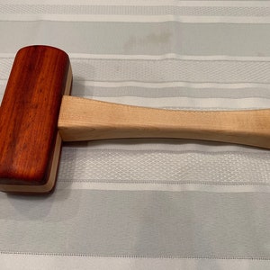 May include: A wooden mallet with a red and natural wood finish. The mallet has a rounded head and a long handle.
