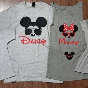 May include: A set of four gray t-shirts featuring a cartoon Mickey Mouse and Minnie Mouse design. The shirts have the words "Daddy", "Mommy", "Winnie", and "Lincoln" printed on them.