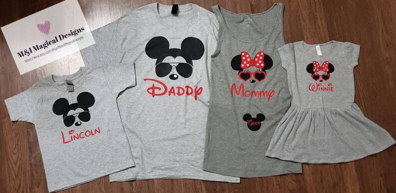 May include: A set of four gray t-shirts featuring a cartoon Mickey Mouse and Minnie Mouse design. The shirts have the words "Daddy", "Mommy", "Winnie", and "Lincoln" printed on them.