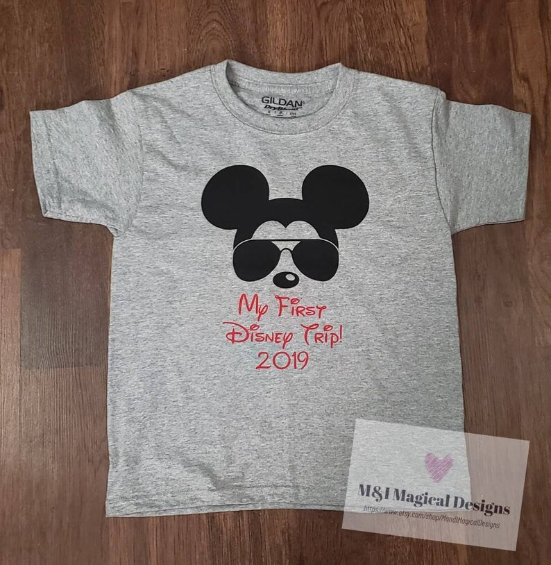 May include: Gray t-shirt with a black Mickey Mouse wearing sunglasses and the text "My First Disney Trip! 2019" in red.