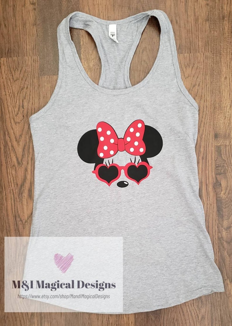May include: Gray tank top with a red and white Minnie Mouse graphic wearing heart-shaped sunglasses. The graphic includes a red bow with white polka dots. The text "M&I Magical Designs" and a website address are printed on the bottom of the shirt.