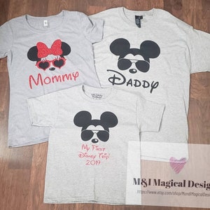 May include: Three gray t-shirts with a Mickey Mouse design. The shirts say "Mommy", "Daddy", and "My First Disney Trip! 2019".