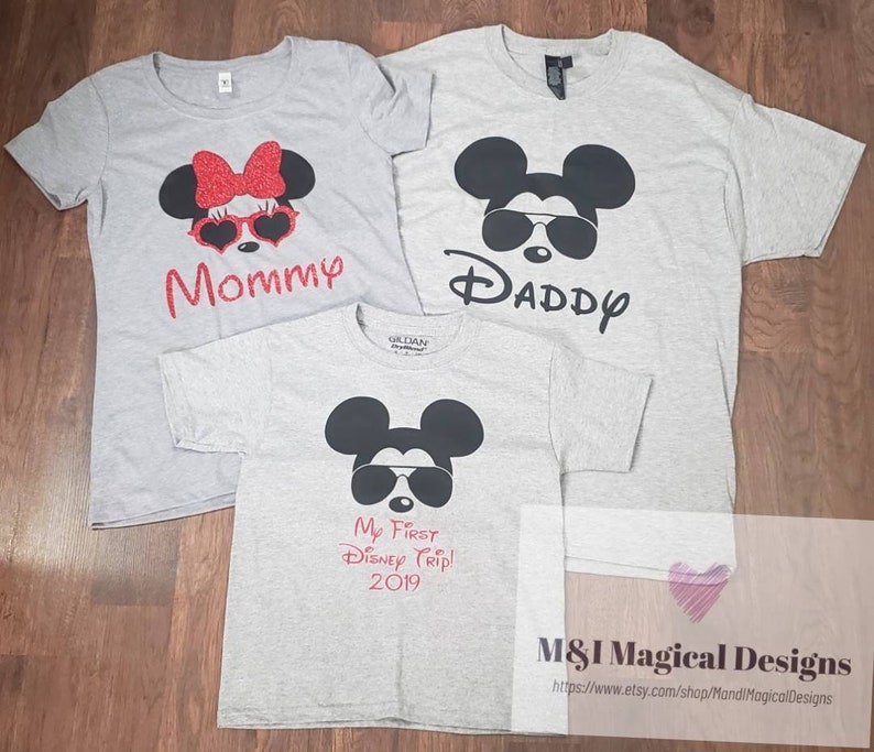 May include: Three gray t-shirts with a Mickey Mouse design. The shirts say "Mommy", "Daddy", and "My First Disney Trip! 2019".