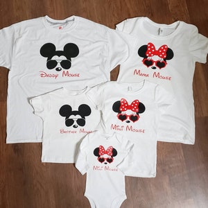 May include: Set of four white t-shirts with a Mickey Mouse and Minnie Mouse theme. The shirts feature images of Mickey and Minnie Mouse wearing sunglasses and have the text "Daddy Mouse", "Mama Mouse", "Brother Mouse", and "Mini Mouse".