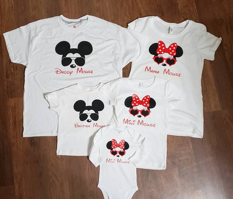 May include: Set of four white t-shirts with a Mickey Mouse and Minnie Mouse theme. The shirts feature images of Mickey and Minnie Mouse wearing sunglasses and have the text "Daddy Mouse", "Mama Mouse", "Brother Mouse", and "Mini Mouse".
