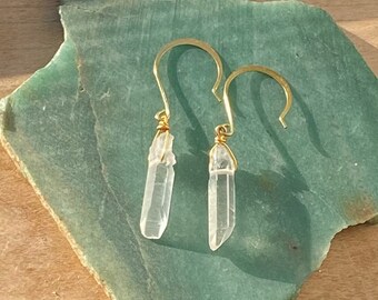 May include: A pair of gold earrings with clear quartz crystal drops. The earrings are simple and elegant, perfect for everyday wear.