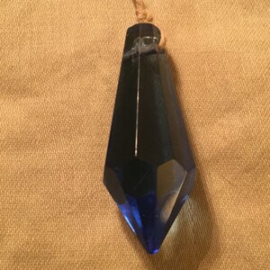 May include: A dark blue crystal pendant with a faceted design hangs from a brown cord.