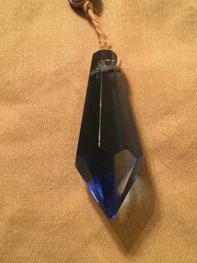 May include: A dark blue crystal pendant with a faceted design hangs from a brown cord.