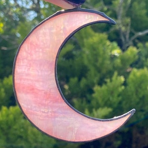 May include: A pink stained glass crescent moon with a black outline.