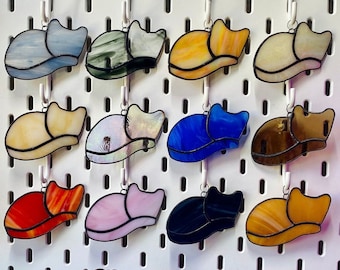 May include: A collection of 12 stained glass cat ornaments in various colors, including blue, red, green, yellow, and brown. Each ornament features a cat sleeping in a curled-up position.