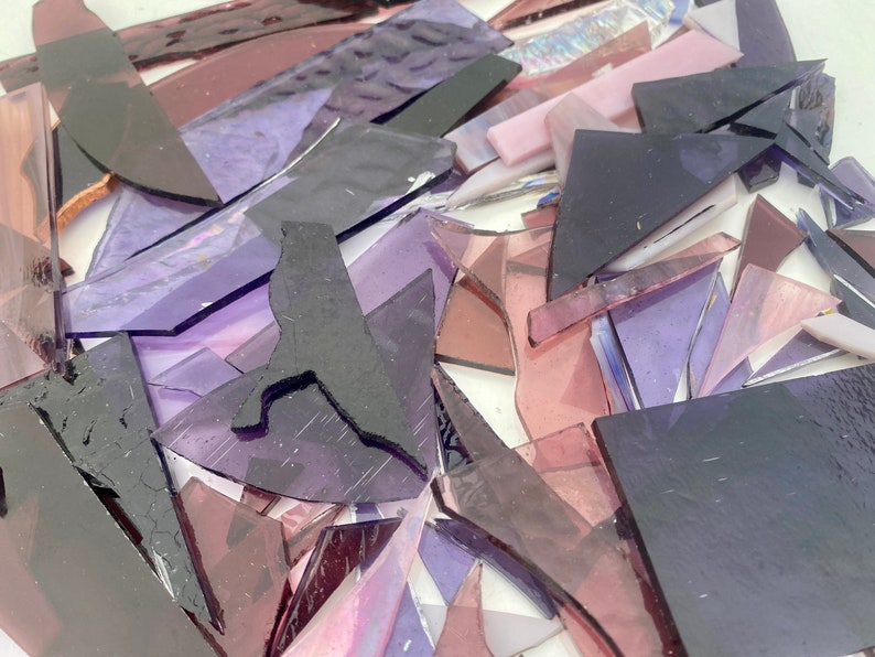 May include: A pile of purple and pink glass shards, some with iridescent finishes, for crafting or mosaic projects.