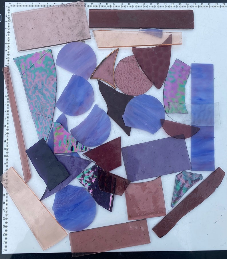 May include: Assortment of purple, pink, and brown stained glass pieces in various shapes and sizes, including circles, triangles, and rectangles.