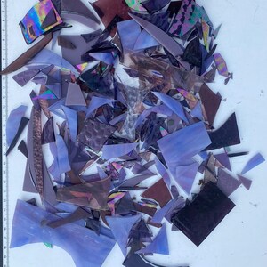 May include: A collection of purple, iridescent, and black glass shards. The shards are various shapes and sizes, and some have a textured surface.