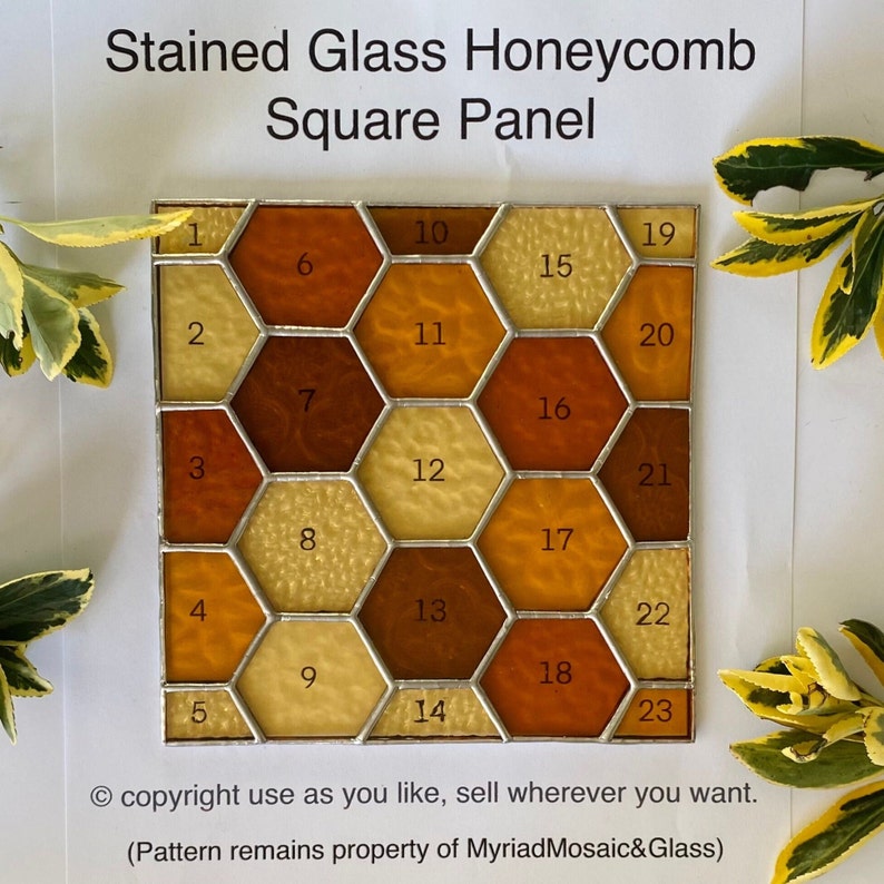 K&ouml;nnte beinhalten: Ein quadratisches Glasmosaik-Honigwabenpanel mit 23 einzelnen sechseckigen Teilen in Braun- und Gelbt&ouml;nen. Jedes Teil ist von 1 bis 23 nummeriert. Das Panel ist in Silber gerahmt.
