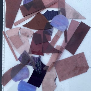 May include: A collection of purple and blue glass pieces in various shapes and sizes. The glass pieces are arranged on a white surface.