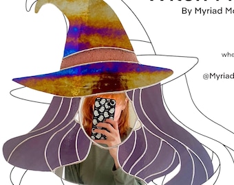 Puede incluir: Un espejo de vidrio coloreado con forma de bruja con una peluca morada y un gran sombrero iridiscente. El espejo refleja a una persona sosteniendo un teléfono con un patrón de fantasma.