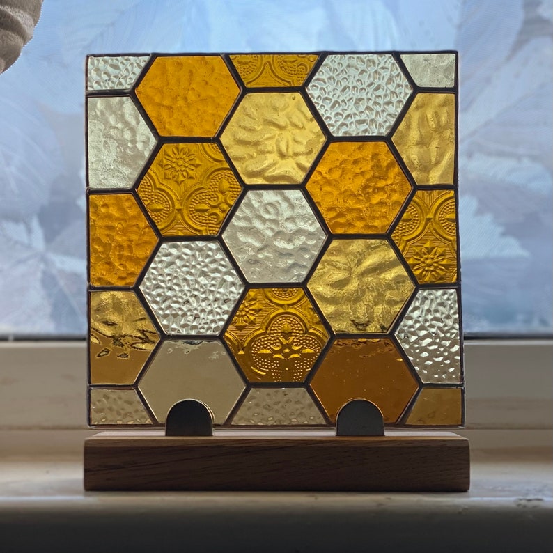 K&ouml;nnte beinhalten: Ein Buntglasfenster mit einem Wabenmuster. Das Fenster besteht aus kleinen, einzelnen Glasscheiben in Gelb-, Gold- und Wei&szlig;t&ouml;nen. Das Fenster ist auf einem Holzrahmen montiert.