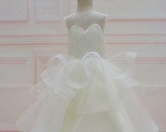 May include: A white tulle dress with a sweetheart neckline and multiple layers of ruffles. The dress is on a wooden mannequin.