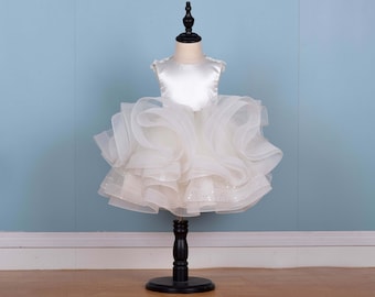 May include: A white tulle dress with a satin bodice and a ruffled skirt. The dress is on a black stand.