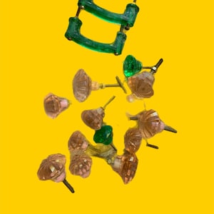 Peut inclure: Un assortiment de boutons et de poignées de placard en verre vintage de différentes couleurs. La collection comprend des boutons verts, roses et ambrés et deux poignées vertes. La quincaillerie est posée sur un fond jaune vif.