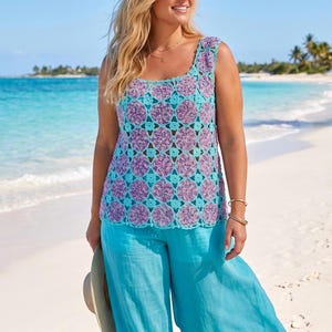 Op de afbeelding: Een mouwloze gehaakte top met een herhalend patroon van cirkelvormige paarse en roze gemêleerde garenmotieven verbonden door helder turquoise randen, gecombineerd met een wijde turquoise broek en een strooien hoed met brede rand.