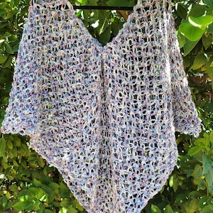 Może przedstawiać: Szal wykonany na szydełku w jasnofioletowym i białym kolorze. Szal wykonany jest delikatnym wzorem ażurowym i ma trójkątny kształt.