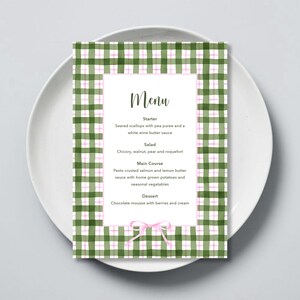 Op de afbeelding: Een groene en roze ruitjespatroon menukaart met het woord "Menu" in zwarte tekst. Het menu bevat een voorgerecht, een salade, een hoofdgerecht en een dessert.