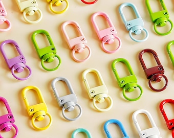 Puede incluir: Surtido de llaveros coloridos con cierre giratorio y un anillo decorativo. Los llaveros son de metal y vienen en una variedad de colores, incluyendo rojo, azul, verde, amarillo, morado y rosa.