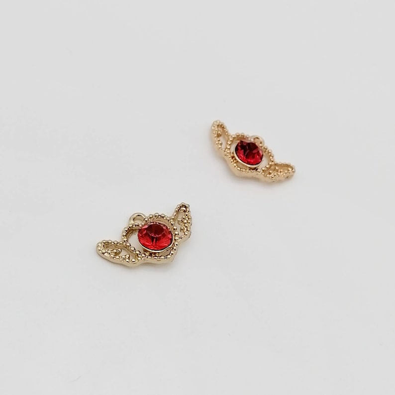 Delicate brass cherub wing pendant with sparkling red ruby crystal accent.