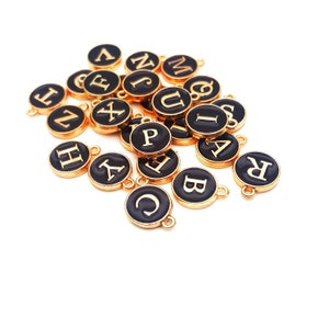May include: A collection of gold-colored metal charms with black enamel and white letters spelling out the alphabet. Each charm has a loop for attaching to a necklace, bracelet, or other jewelry.