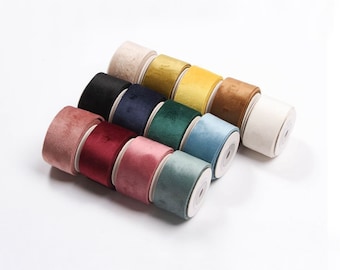 May include: An assortment of velvet ribbon rolls in various colors, including pink, burgundy, black, navy, teal, and gold. The rolls are neatly arranged, showcasing the texture and color variations of the fabric. The ribbon is likely used for crafts, gift wrapping, or decorative purposes.