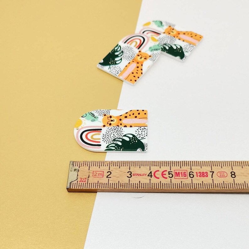 K&ouml;nnte beinhalten: Drei wei&szlig;e Acrylformen mit einem bunten Muster aus Geparden, Regenbogen und gr&uuml;nen Bl&auml;ttern. Die Formen sind etwa 7,6 cm lang und 5,1 cm breit.