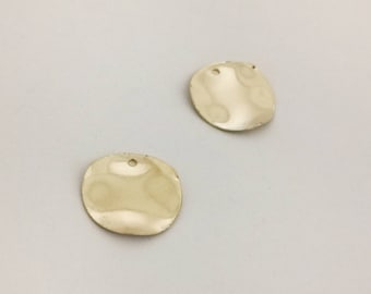 以下が含まれることがあります： 中央に穴が開いた金色の金属製の円が2つ。円はわずかに不均一で、ハンマーで叩いたような質感がある。