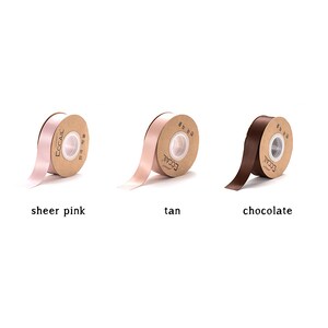 May include: Three spools of ribbon in different colors: sheer pink, tan, and chocolate. Each spool is wrapped in brown paper with the word "ECCAIL" printed on it.