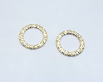 May include: Two gold-coloured, hammered-texture circle charms with small holes at the top for jewellery making. The charms are round with a textured surface and a shiny finish. They are displayed on a white background.