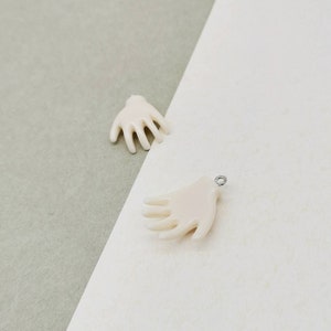 May include: Two white hand-shaped resin charms, one with a silver loop for hanging. The charms have a smooth, matte finish.