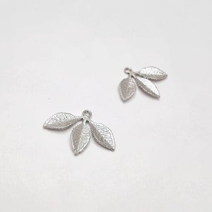 May include: Two silver leaf charms with three leaves each. The leaves have a textured surface and are connected to a loop at the top.