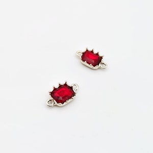 May include: Two silver-toned connector charms with red, faceted, rectangular gems. The gems are set in a crown-like design.